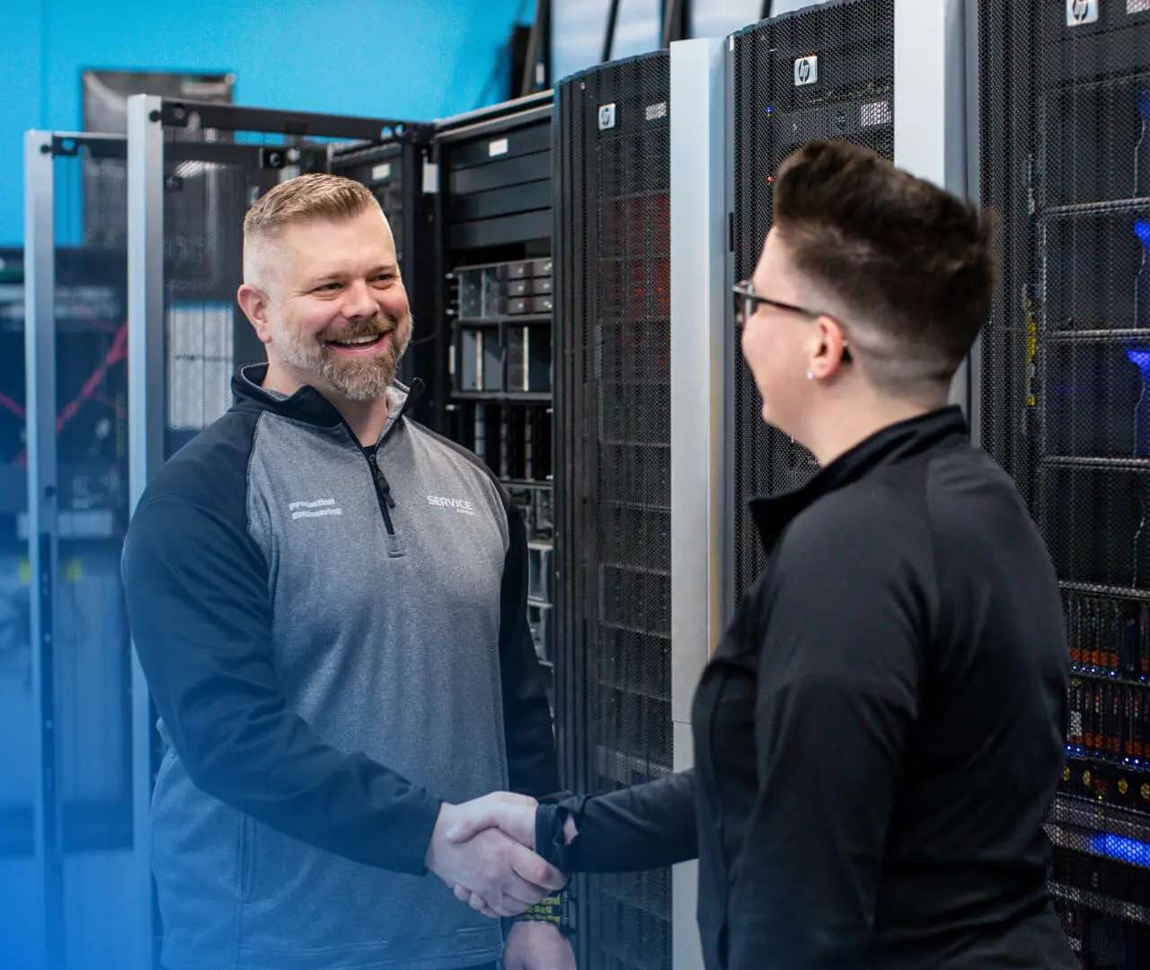 An image of two engineers shaking hands inside a data center in front of large equipment racks