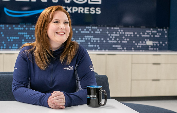 An image of a smiling female employee sitting at a table wearing a Service Express quarter zip with a coffee mug next to her