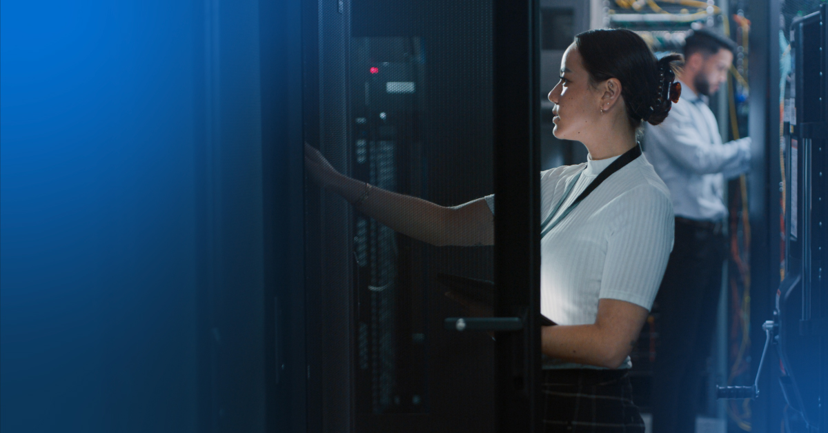 An image of a female engineer reaching into a server rack, a male engineer is also working on equipment in the background