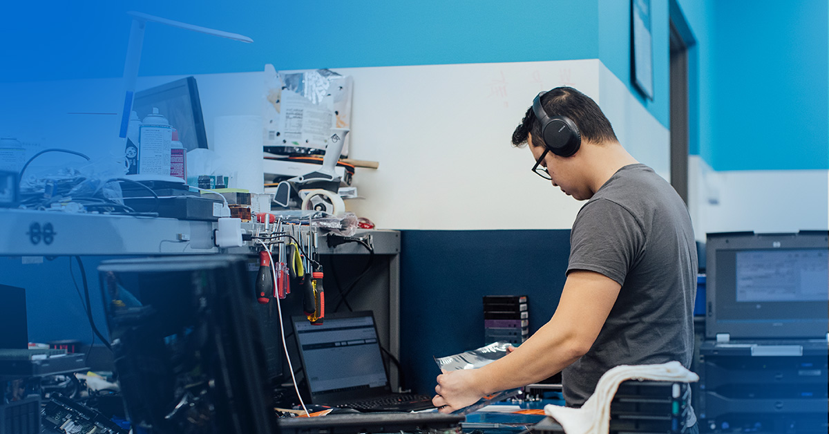 An image of a male engineer wearing headphones at a workbench testing parts