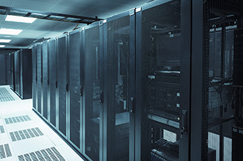 An image of a row of equipment racks in a data center under fluorescent lights