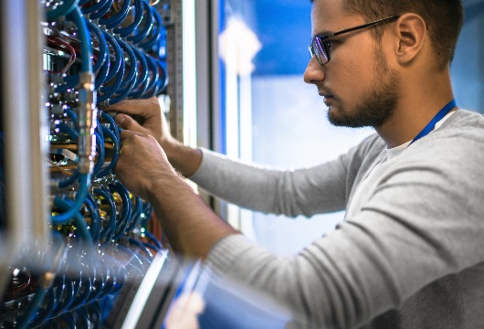 Young man connecting cables in server cabinet while working in data center