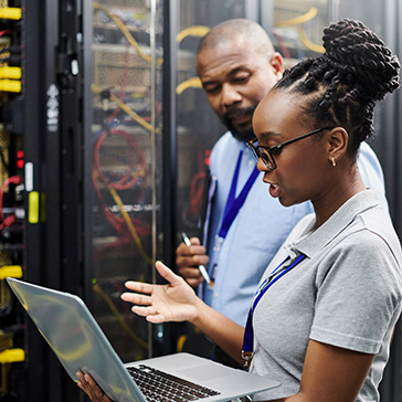 An image of a female engineer holding a laptop and speaking with a male engineer in front of equipment in a data center