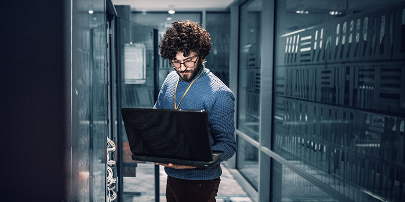 An image of a male engineer holding a laptop in a data center