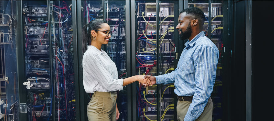 An image of a female and male engineer in a data center shaking hands