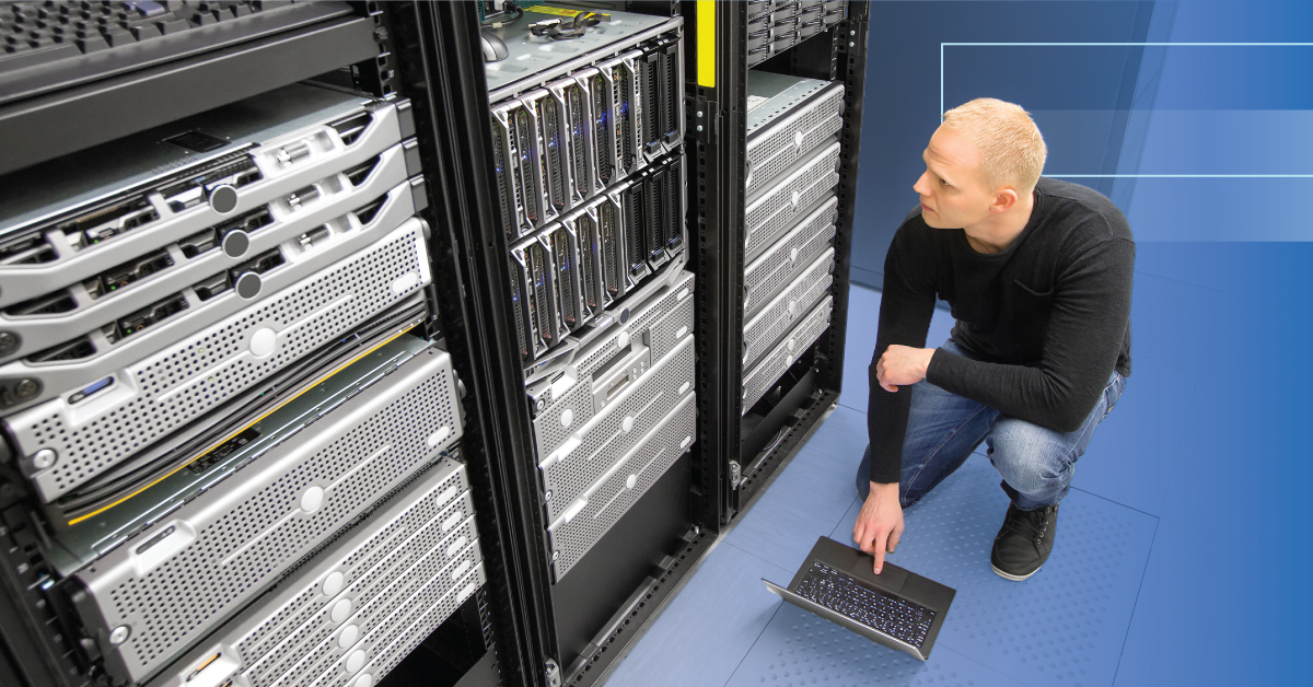 Man keeling down in data center, reaching for laptop