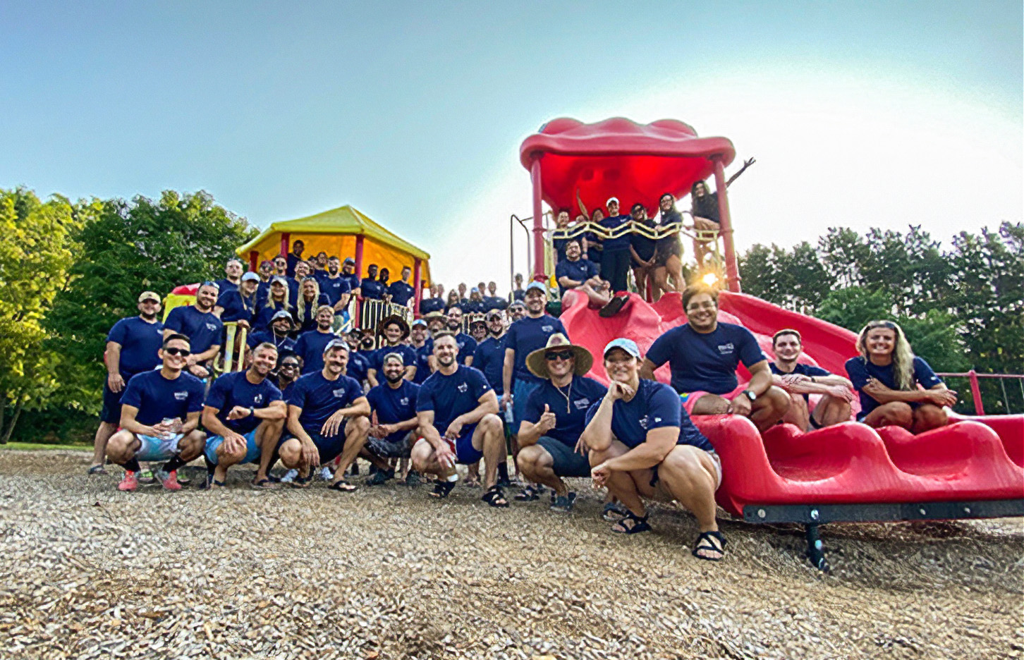 A photo of a large group, all with dark blue shirts, posing on playground equipment