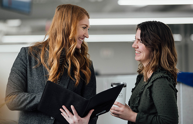 An image of two female coworkers in an office conversing and smiling