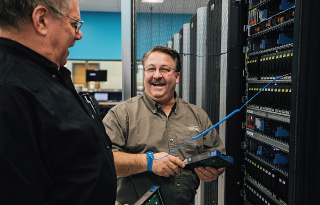 An image of two male engineers working in a data center laughing, smiling