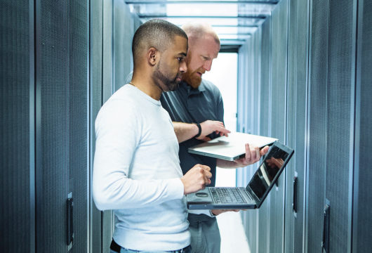 An image of two male engineers holding laptops in a data center