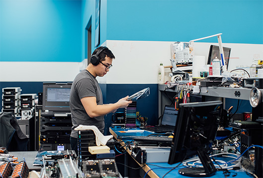 An image of a male engineer wearing headphones in the lab inspecting equipment parts