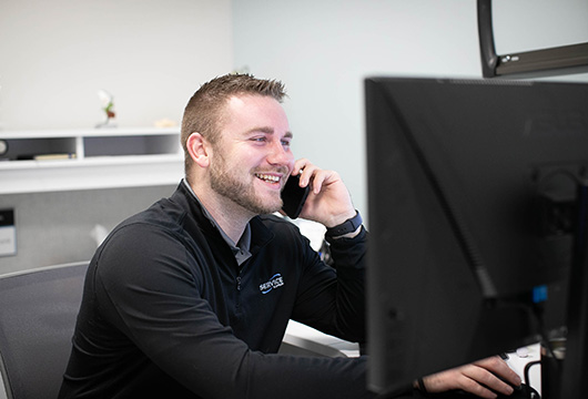 An image of a Service Express employee smiling and talking on the phone at their desk