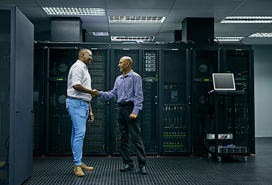 An image of two male engineers shaking hands in front of servers in a data center