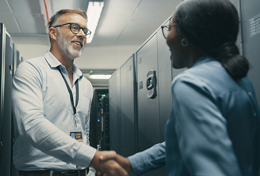 An image of a male engineer shaking hands with a female engineer in a data center