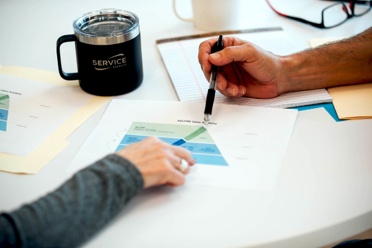 An image of two hands, one holding a pen pointing to a graph on a paper in front of a Service Express mug